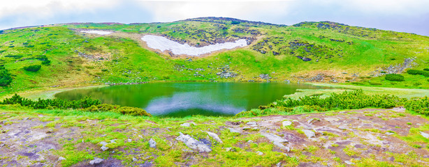 Alpine lake among the mountain peaks in the spring, snow and cloudy weather