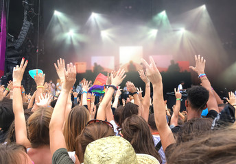 Crowd audience with hands raised at a rock music festival or concert, blurred stage lights in the...