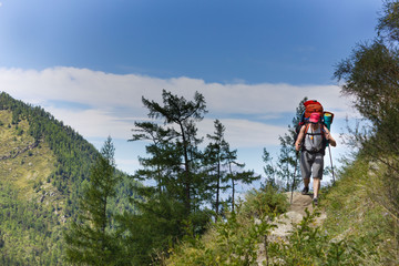 Fototapeta na wymiar A man with a backpack and trekking sticks walks along the mountain trail