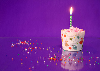 One birthday cup cake and candle on the purple background with colorful rounded sugar beads.