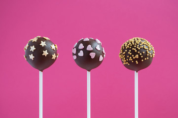 Chocolate cake pops decorated with gold confectionery sprinkles In the form of heart, star and ball on a pink background. Picture for a menu or a confectionery catalog.
