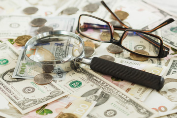 Different coins and banknotes with a magnifying glass and glasses