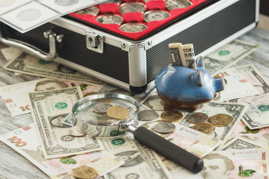 Different coins and banknotes with a magnifying glass and piggy bank