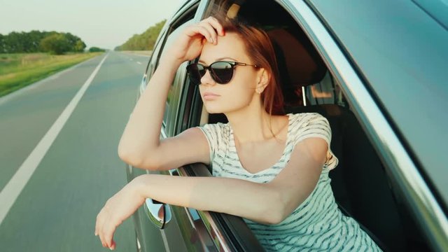 Sexy young woman rides in a car, peeks out of the window. Beautiful light before sunset. Slow motion 4k video