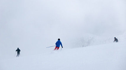 Naklejka na ściany i meble Skiers in thick fog on ski slope in ski resort.