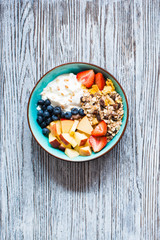 Healthy breakfast, cereal with yogurt, strawberries, blueberry, apple, banana, on rustic wooden.  Top view