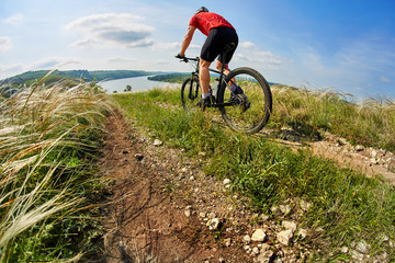Fototapeta premium Young cyclist riding mountain bicycle through green meadow against beautiful sky.