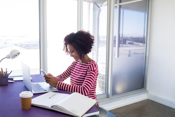 Female executive using mobile phone while working over laptop