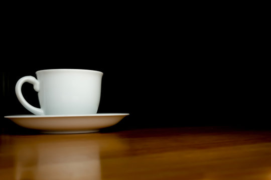 A white cup of coffee in the dark background on wood table.