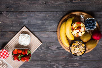 Healthy breakfast, cereal with yogurt, strawberries, blueberry, apple, banana, on rustic wooden.  Top view