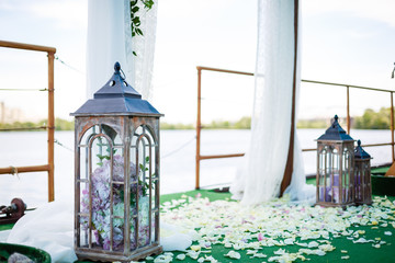 Wedding decor in rustic style.Two white vintage lamp with flowers inside standing on green grass