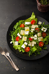 Fresh salad with cherry, arugula, feta, basil and olive oil in a plate