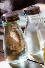 Old fashion glass peppercorns and salt shaker on rustic wooden table at window