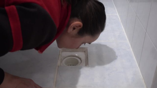 4K Woman smells drain hole in floor at home
