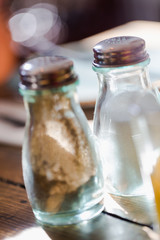 Old fashion glass peppercorns and salt shaker on rustic wooden table