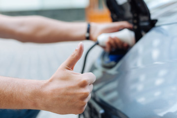 Male hand showing thumbs-up while charging an e-car