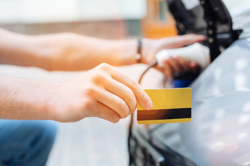Male hand holding a credit card while charging an electric car