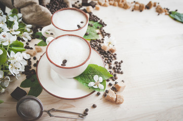 Two cups of freshly brewed, frothy cappuccino. Spilled coffee grains, chocolate and cane sugar. Theme of coffee, cappuccino, mocha chino, america no. Beautiful elegant background with place for text

