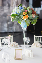 Table set for wedding banquet with floral composition of roses and hydrangea. Flower decoration in tall vase.