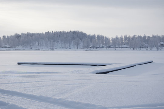 Beautiful winter specific photo. Frozen lake at wintertime. Photo with beautiful forest in the background and a dock lying in the middle of the lake.