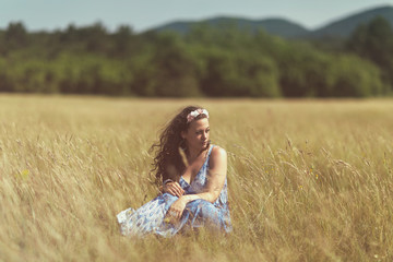 Fototapeta na wymiar Portrait of a beautiful woman with long hair wearing fantasy blue silk sitting in the yellow field. Copy space. Outdoor shot