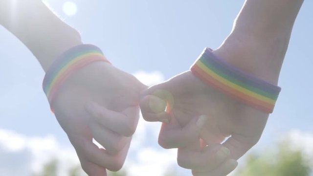 Close up of couple with rainbow wristbands holding hands