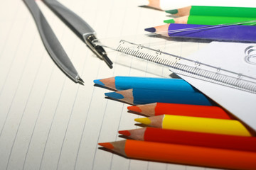 Photo of crayons with ruler and compass on exercise book and a paper