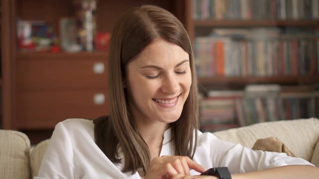 Woman at home texting on smart watch. Beautiful young female professional working on smartwatch