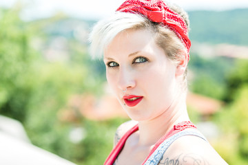 Young blonde pinup girl with a red bow in her hair posing in the park. Concept pinup woman.