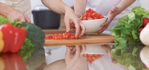 Close-up of four human hands are cooking in a kitchen. Friends having fun while preparing fresh...