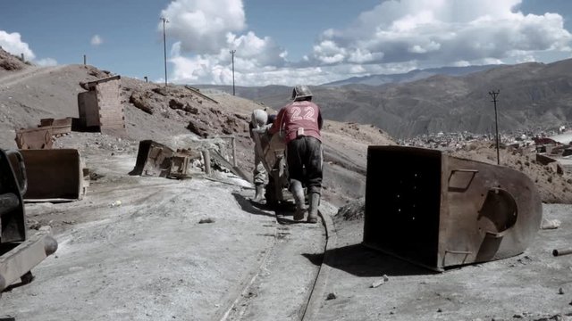 Couple of miners pushing a cart full of mineral passing through the tunnel. Bolivia
