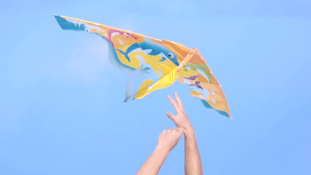 Detail of hands trying to reach the kite that flies on a blue sky