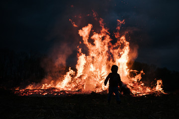 Boy stands in front of a massive fire