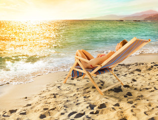 Fototapeta na wymiar Girl tans on a deck chair on a beautiful beach