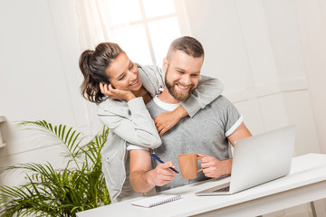 happy woman hugging man that sitting at workplace at home
