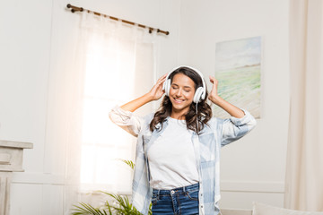 Happy young woman wearing headphones listening music at home