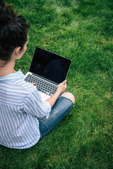 Cropped shot of brunette girl using laptop with blank screen while sitting on grass