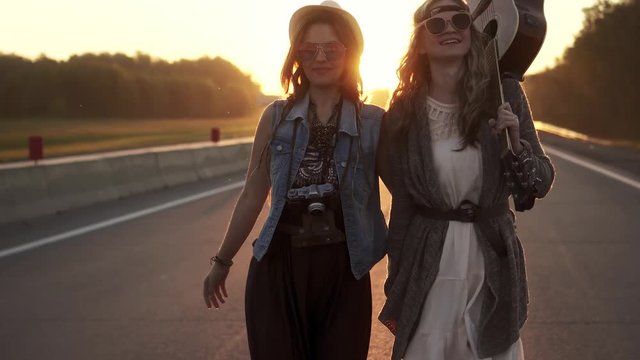 Two hippie girls walk along the freeway at dawn