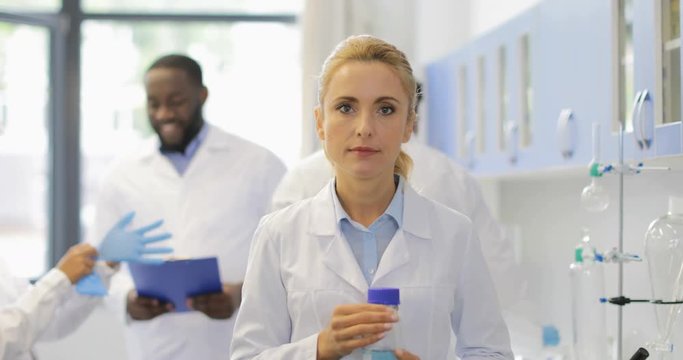 Scientist Woman Hold Bottle With Chemical Liquid Happy Smiling Over Talking Researchers Mix Race Team In Modern Laboratory Slow Motion 60