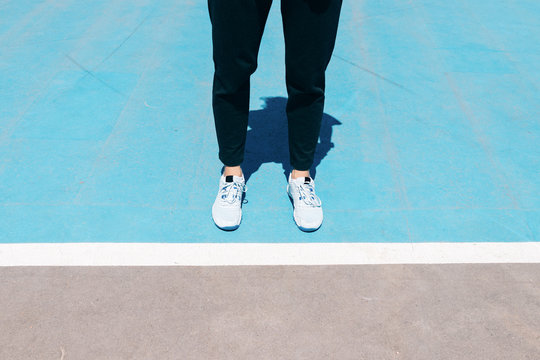 Cropped image of female legs in sneakers and black pants are on a blue sports field in front of the white line