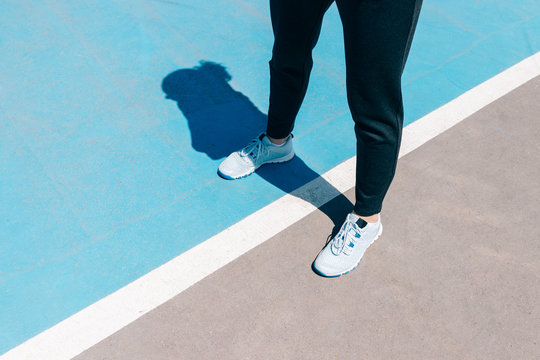 Cropped image of female legs in sneakers and black pants standing on a blue sports field