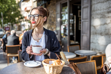 Fototapeta na wymiar Young woman having a breakfast with coffee and croissant sitting outdoors at the french cafe in Lyon city