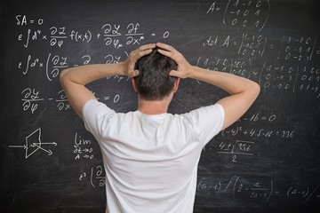 Young man is solving mathematical problem on blackboard and is confused.
