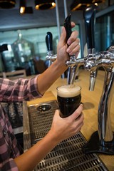 Cropped hands of barmaid pouring drink from tap 