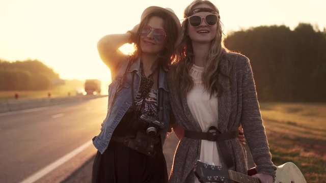 Two hippie girls walk along the freeway at dawn