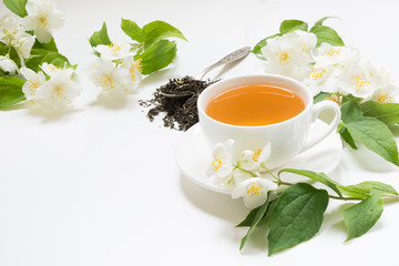 Jasmine dry green tea leaves with fresh jasmine flowers and cup of tea on white background. Space...
