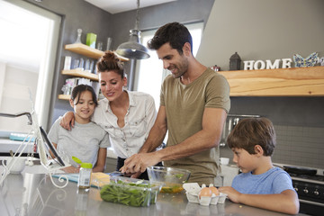 Family In Kitchen Following Recipe On Digital Tablet Together