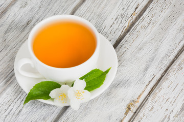 Jasmine flowers and cup of green tea on wooden background.