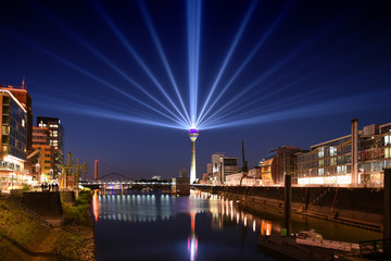 panoramic skyline view Duesseldorf, Germany - media habor district during sunset with iluminated rhine tower and huge laser rays into the sky