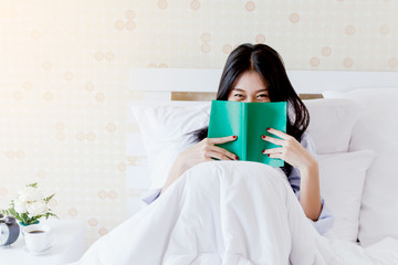 Young beautiful asia woman reading book on bed